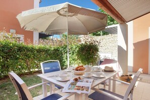 Eine Terrasse im Freien mit einem Tisch, der für eine Mahlzeit gedeckt ist, inklusive Teller, Gläsern und einem Brotkorb.
