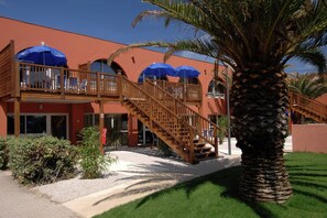 Ein Hotel mit roter Fassade, hölzernen Balkonen und blauen Sonnenschirmen.