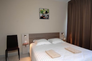 Ein Hotelzimmer mit einem Bett, zwei Kissen, einem Sessel, einem Nachttisch mit Lampe und einem Wandbild.