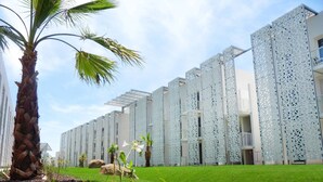 A modern building with a patterned facade, a palm tree, and a well-maintained lawn. - Maisonette in France with Terrace (Cap d'Agde)