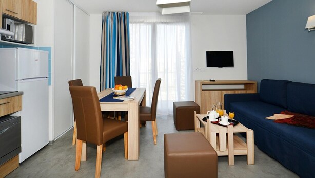 A modern hotel room with a dining area, kitchenette, and a living space with a sofa and TV. - Maisonette in France with Terrace (Cap d'Agde)