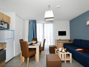 A modern hotel room with a dining area, kitchenette, and a living space with a sofa and TV.