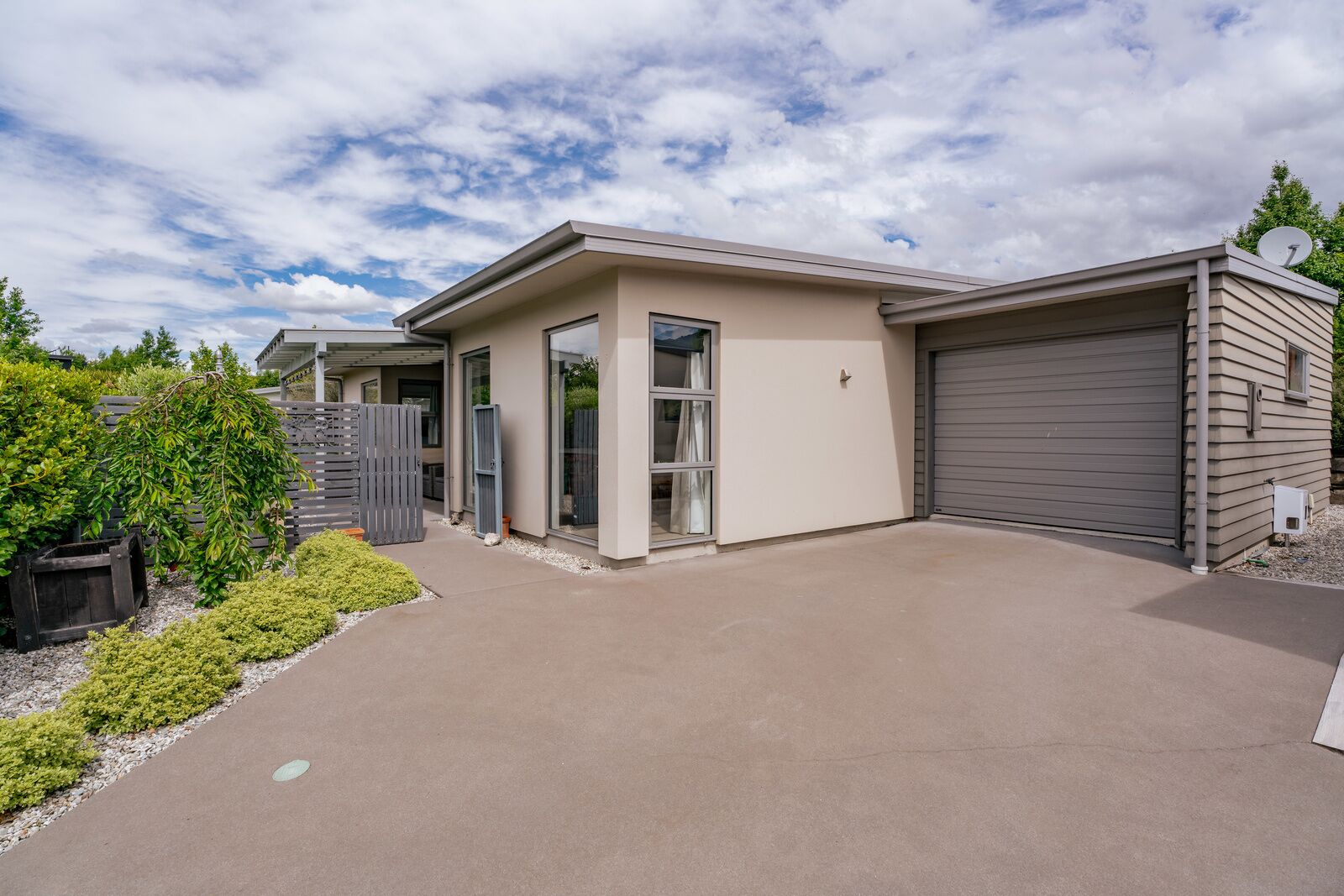 Une maison moderne de plain-pied avec un garage, un patio couvert et un petit jardin.