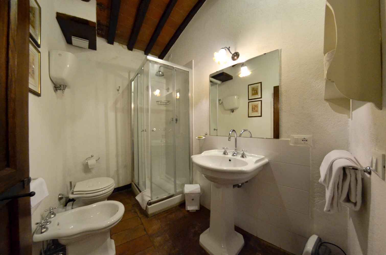 A bathroom with a glass-enclosed shower, a pedestal sink, a bidet, and a toilet.