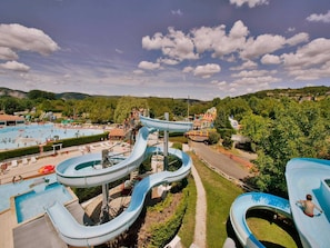 A water park with multiple slides and pools, surrounded by greenery and hills.
