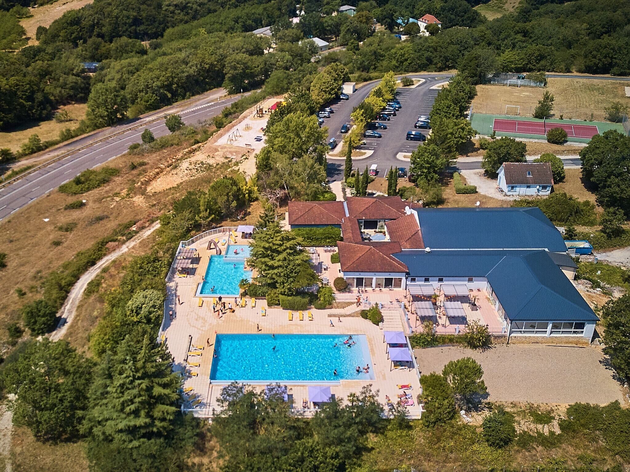 Luftaufnahme eines Resorts mit großem Schwimmbecken, mehreren Gebäuden und einem Parkplatz.