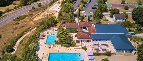 An aerial view of a resort with a large swimming pool, multiple buildings, and a parking area.