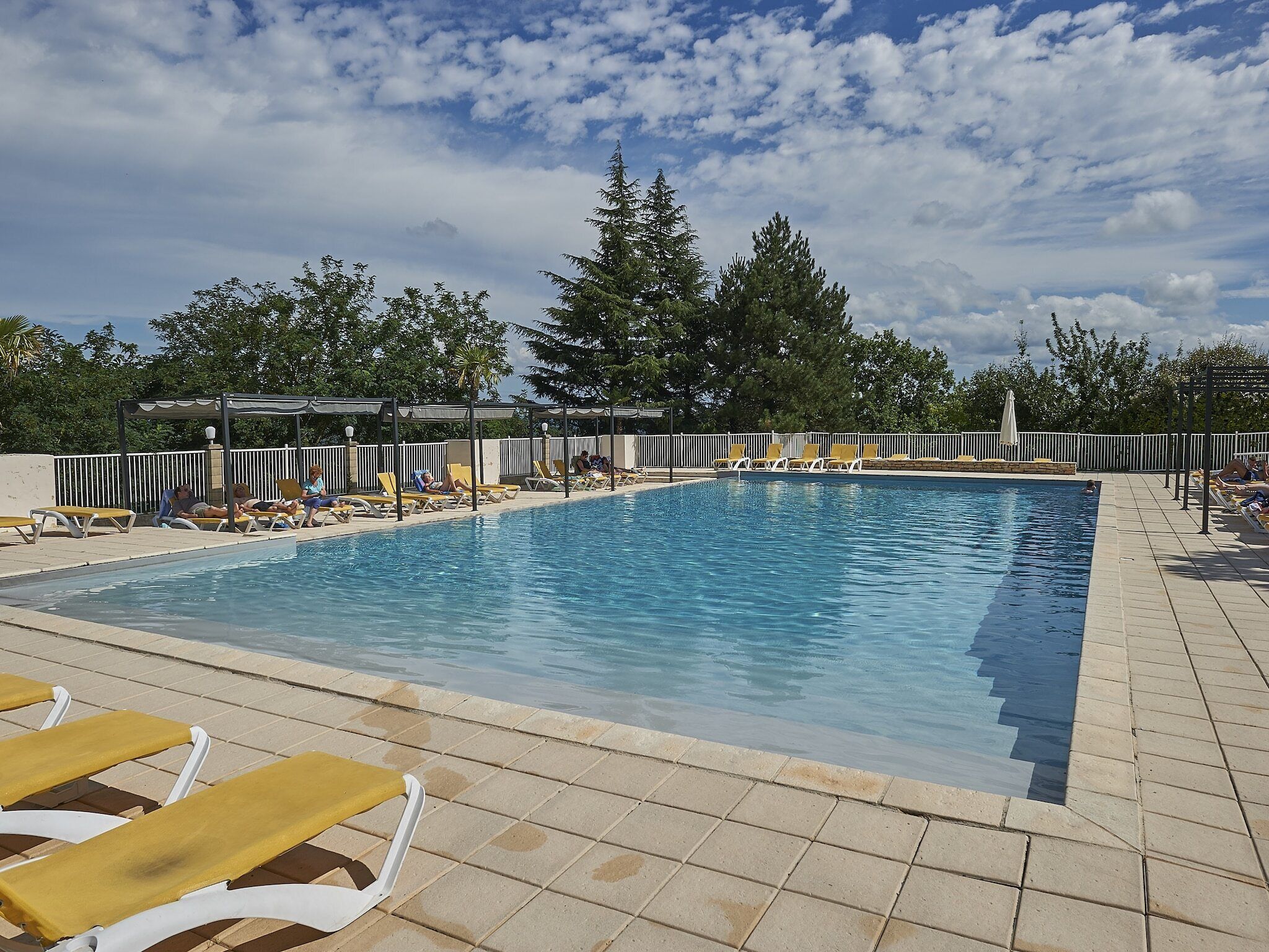 A rectangular pool with tiled edges, surrounded by lounge chairs and umbrellas.