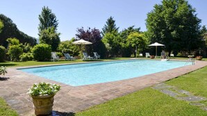 Ein rechteckiger Pool mit Backsteinrand, umgeben von einer grünen Rasenfläche und Bäumen.