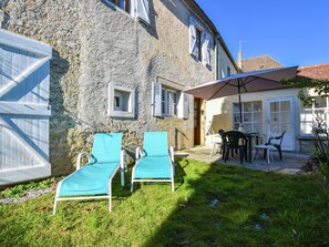 Ein Steinhaus mit einer Terrasse, auf der zwei blaue Liegestühle und ein Tisch mit Stühlen stehen.
