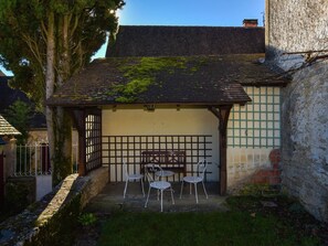 Ein kleines, rustikales Gebäude mit Ziegeldach und einer überdachten Terrasse mit Metallstühlen und einem Tisch.
