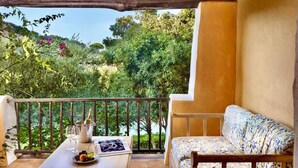 A balcony with a wooden table, a cushioned bench, and a view of a lush garden and hills. - Holiday apartment mit Klimaanlage und Pool (Liscia di Vacca)