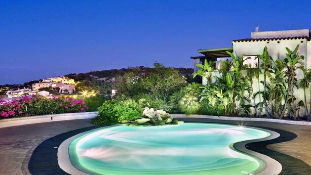 A swimming pool with a wavy edge, surrounded by a wooden deck and lush greenery. - Holiday apartment mit Klimaanlage und Pool (Liscia di Vacca)