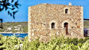A stone building with arched windows and a door, surrounded by greenery and overlooking a coastal area. - Holiday apartment mit Klimaanlage und Pool (Liscia di Vacca)