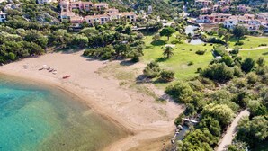 An aerial view of a coastal area with a beach, clear waters, and a cluster of buildings with balconies overlooking the beach. - Holiday apartment mit Klimaanlage und Pool (Liscia di Vacca)