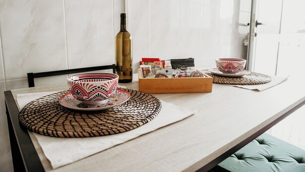 A table with a woven placemat, a bottle, a box of snacks, and a cup on a saucer.