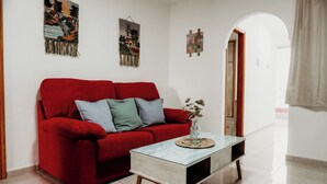 A red sofa with cushions, a glass coffee table with a vase, and wall art.