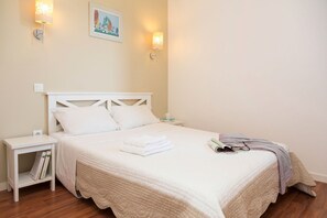 A neatly made bed with white linens, a bedside table with books, and a wall-mounted lamp. - Apartment in Guidel by the Seafront (Guidel)