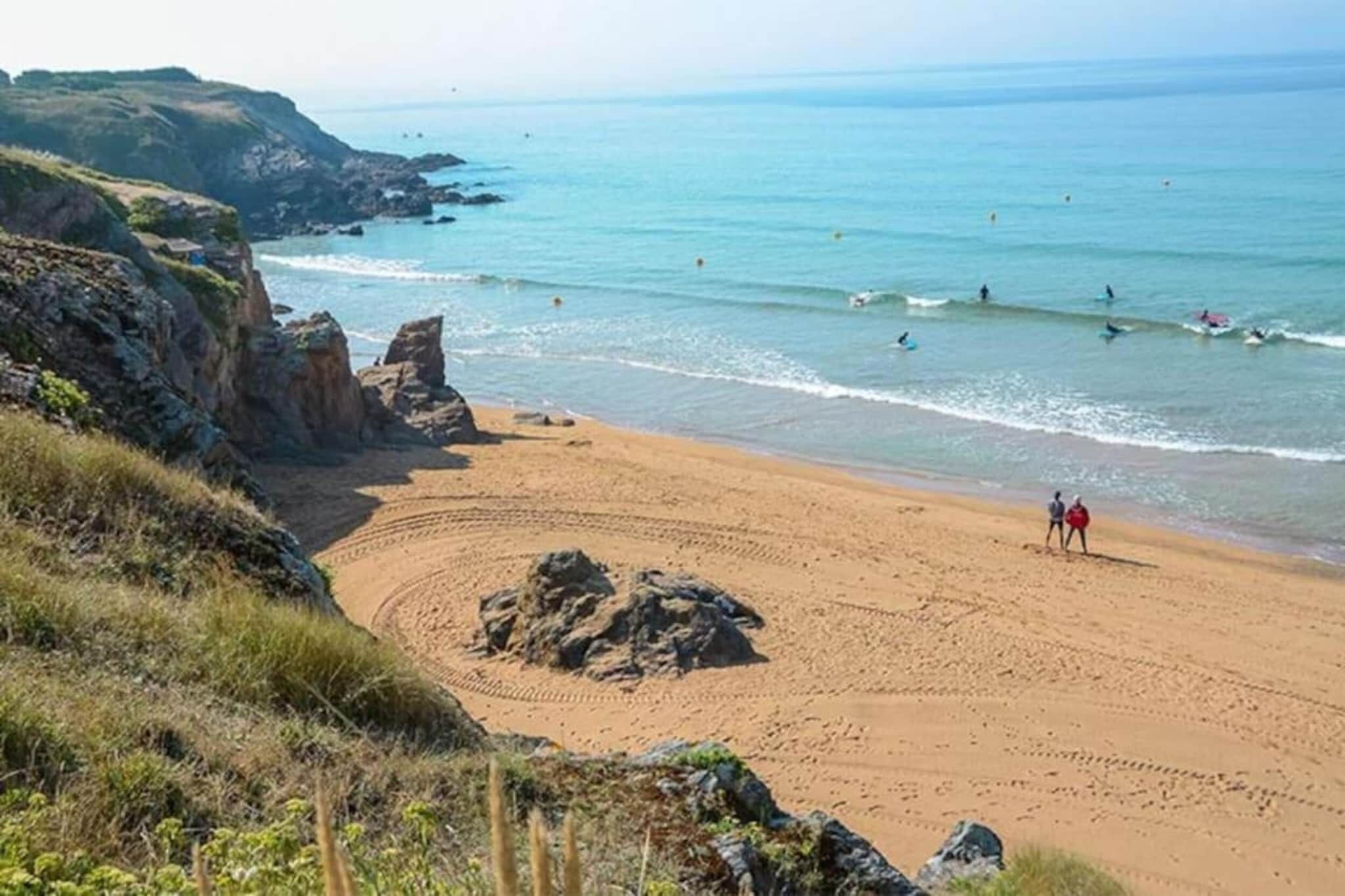 A beach with a rocky outcrop, a sandy area with footprints, and the ocean in the background.