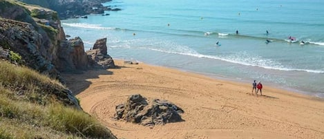 Una playa con un promontorio rocoso, una zona arenosa con huellas, y el océano al fondo.