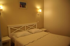 A single bed with a white headboard and two bedside tables, each with a wall-mounted light.