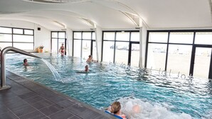 En indendørs swimmingpool med klare vinduer, flisegulv og en person i vandet.