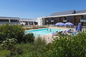 A swimming pool with lounge chairs and umbrellas, surrounded by greenery and modern buildings.