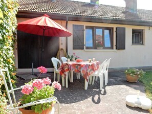 Une terrasse extérieure avec une table et des chaises, un parasol rouge et des plantes en pot.