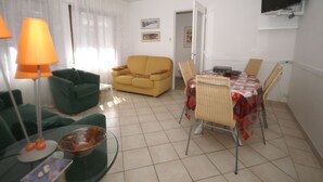A living room with a sofa, a dining table with chairs, a TV mounted on the wall, and a lamp. - Holiday home in Vic-sur-Seille near the forest (Vic-Sur-Seille)