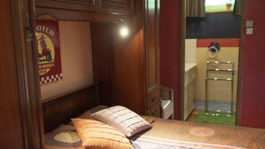 A compact bedroom with a bed, pillows, a poster, and a small dresser.