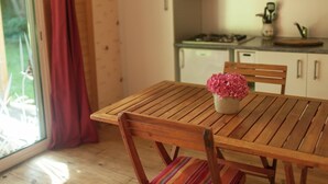 A wooden dining table with a potted plant, a window with a view of greenery, and a kitchen area with cabinets and appliances.