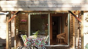 A wooden deck with a table covered in a floral tablecloth, surrounded by chairs.