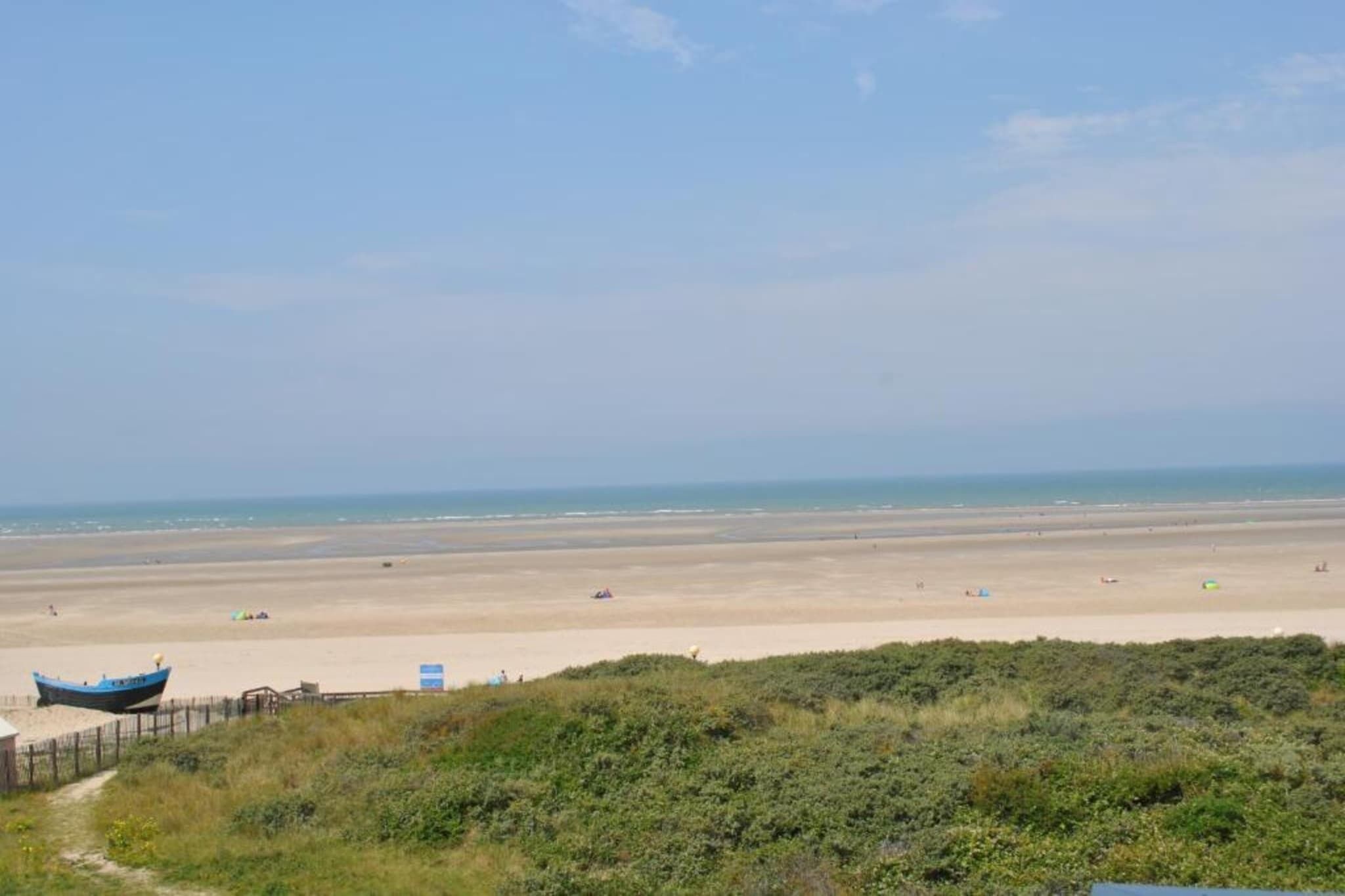 Una playa con un bote, un sendero y algo de vegetación al frente.