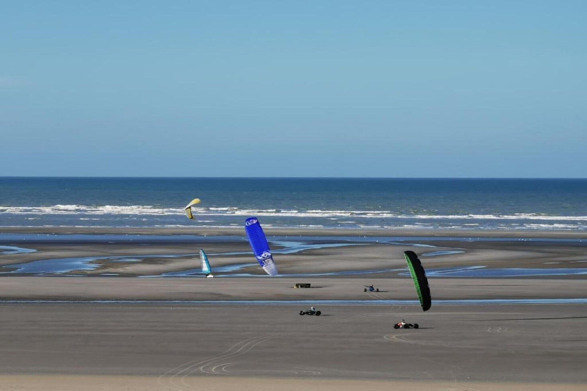 A beach with multiple kites and a sailboat.
