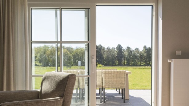 Una habitación con un gran ventanal corredero que da a un patio exterior con muebles de mimbre y vistas a un paisaje verde.