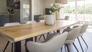 Una cocina moderna con una mesa de comedor de madera, sillas blancas y luces colgantes.