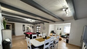 En rummelig opholdsstue med et billardbord, et spisebord med stole og en sofa.