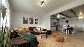 En moderne stue med en brun lædersofa, et spisebord med stole, og et køkken i baggrunden.