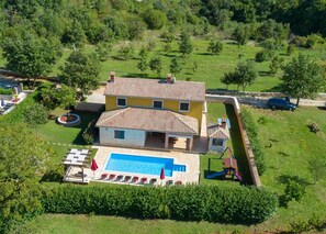 A two-story house with a swimming pool, surrounded by a well-maintained lawn and trees.