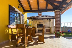 Une terrasse extérieure avec une cheminée en pierre, des chaises en bois et un mur jaune.