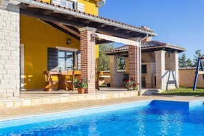 Un espace aménagé au bord de la piscine, avec une terrasse en briques, des sièges d’extérieur et une piscine.
