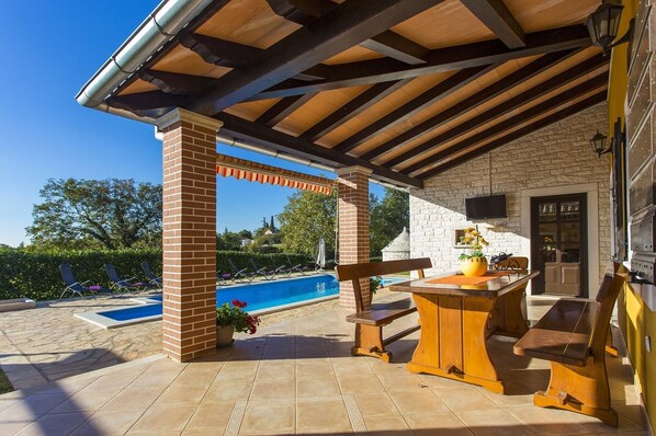 An outdoor patio with a pool, a stone wall, and a wooden table with chairs.