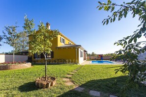 A yellow house with a swimming pool and a small tree in the yard.