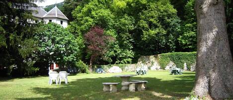 A serene garden with a white building, stone benches, and lush greenery.