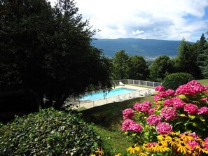 Una piscina rodeada de exuberante vegetación y flores rosadas, con vistas a montañas distantes.
