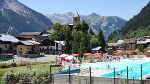 Zona de piscina con montañas al fondo, rodeada de edificios y árboles.