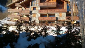 Una cabaña de madera de varios pisos con balcones, muros de piedra y un paisaje nevado al fondo.