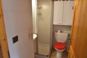 Bathroom features a shower enclosure, toilet, and storage shelf.