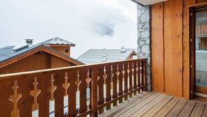 A wooden balcony with a stone wall and a view of neighboring buildings. - Magnificent chalet with balcony (Champagny en Vanoise)