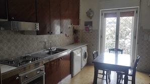 A compact kitchen with a sink, stove, oven, and a washing machine. There is a dining table with chairs and a window with a view of greenery outside. - Apartment between Herculaneum and Pompeii at fields of Vesuvius (Torre del Greco)
